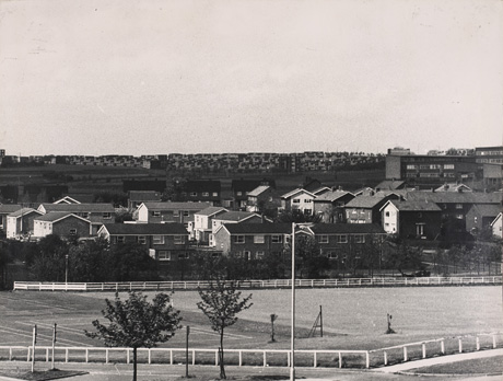 Photograph showing, in the foreground, a tennis court and playing field with approximately thirty semi-detached houses and five two- storeyed blocks of flats, all with pitched roofs, immediately beyond; on the right, the top storeys of a school or college can be seen; in the distance, on the horizon, is a mass of flat-roofed houses; the scene has been described as View From Peterlee Tech. Playing Field, Essington Way
