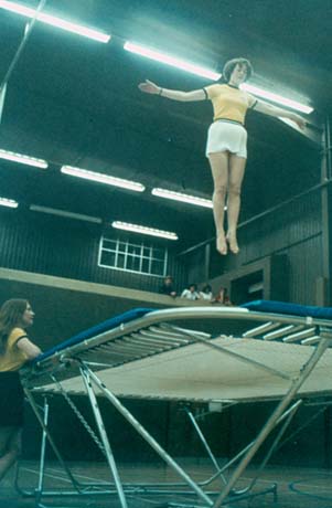Photograph, taken from below, showing a young woman bouncing above a trampoline; the walls and ceiling of the building, which has been identified as Peterlee Leisure Centre can be seen, as can a child leaning on the trampoline and four people looking on from a balcony in the distance