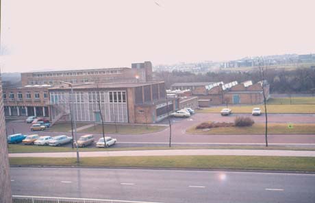 Photograph, taken from above, showing the exterior of brick block of approximately four storeys, surrounded by car parks, in which sixteen cars are parked; a church and houses can be seen hazily in the background; the building has been identified as Peterlee Technical College