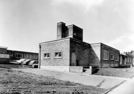Photograph of the exterior of the end and front of a single-storey building of brick, with cars parked behind the building; another building can be seen behind the cars; the photograph has been identified as Health Centre, Peterlee