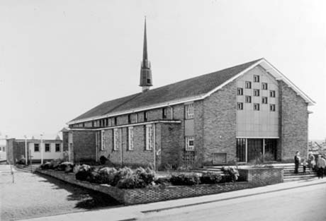 Photograph showing the exterior of the west end and north side of a church with a small garden and indistinct people standing on the steps in front of the west entrance; the church has been identified as St. Cuthbert's Church, Peterlee