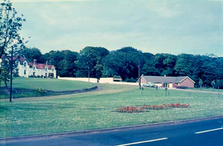 Photograph showing a road, open grassed space, the front of a house with six dormer windows, painted white and the roof of a post-war bungalow; the photograph has been identified as Old Shotton