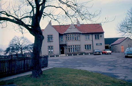 Photograph of the exterior of the front of a large house with a wing on the left and large round bays in the centre of the building, which has been identified as Community Centre, Peterlee; three cars can be seen parked in front of the house, in a yard surfaced with tarmac