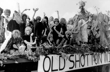 Photograph showing approximately eighteen women and one small girl, aged approximately seven years, dressed as, possibly, cave women and cave men, on the back of a lorry with the words Old Shotton Women's Institute on it, as part of Peterlee Carnival