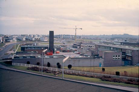Photograph, taken from above, of the exterior of a fire station with a fire tender, a van and cars, in its yard, on the left; on the right is another building of three storeys, which may be a police station; there are other buildings and a crane in the distance; the photograph has been identified as Fire and Police Stations, Peterlee