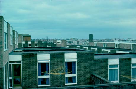 Photograph, taken from above, showing the flat roofs and fronts containing two windows and a door, of linked houses or flats; the roofs of other buildings can be seen in the distance; the photograph has been identified as Brandlings Court, Peterlee