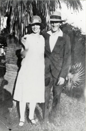 Photograph of a man in a suit, open- necked shirt and large-brimmed hat, standing with a woman in a light dress and a hat with a brim, in front of a palm tree; they have been identified as Mr. and Mrs. Dick, formerly of Seaham, in Australia