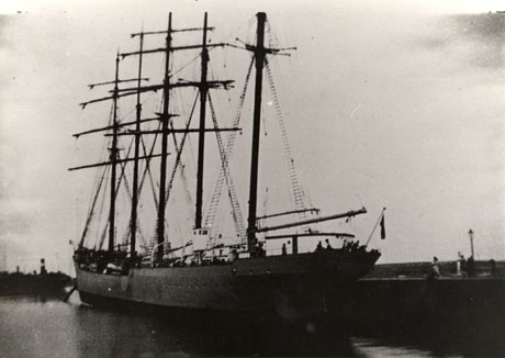 Photograph of a sailing ship with five masts sitting in water near a quay; the ship is photographed from the side and its bows and side can be seen; it has been described as a German training ship in Seaham dock