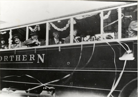 Photograph of the side of a bus showing seven windows decorated with streamers; three men and two women are looking out of the windows; the word Northern can be seen on the side of the bus; the photograph has been identified as Bus Outing Seaham
