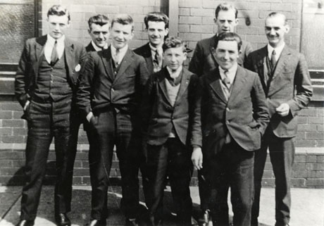 Photograph of six men and two boys posed against a brick wall; all of them are wearing suits and ties; they are identified as the office staff at Dawdon Colliery