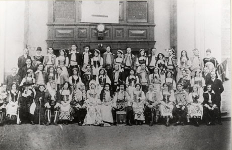 Photograph of the cast in costume of the Seaham Amateur Operatic Society's production of The Gondoliers; they are posed in front of a grand chimney piece; there are approximately fifty members most of whom are dressed as in what appears to be eighteenth century costume