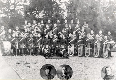 Photograph of forty one members of the Seaham Harbour Salvation Army Band posed in front of trees; there are thirty eight men, most of whom are holding instruments, one woman and two children; all of the people are in uniform; inset are head and shoulders portraits of three men in military uniform, presumably members of the band on active service; the words Seaham Harbour Band 1919 are written on the photograph