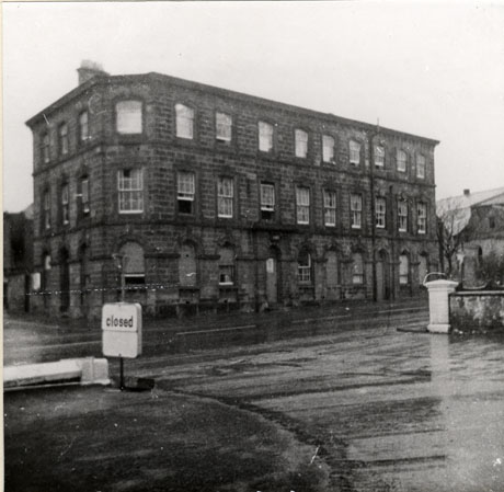Photograph of the exterior of a three storey stone building viewed from across the road in the forecourt of a garage, showing two sides and corner of the building; there are thirteen windows on each floor; the building has been identified as Old Police Station and Magistrates' Court, Tempest Road(Demolished 1975)