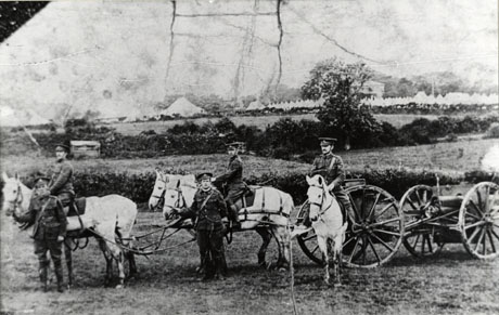 Photograph showing four horses pulling a gun carriage in the foreground of the picture; a soldier is sitting on each of the pairs of horses and a soldier is standing at the head of each of the pairs of horses; another soldier is riding a horse near the gun carriage; in the distance are two fields and hedges and, in the distance, a line of conical tents; the photograph has been identified as Seaham Territorials at Morecambe Bay