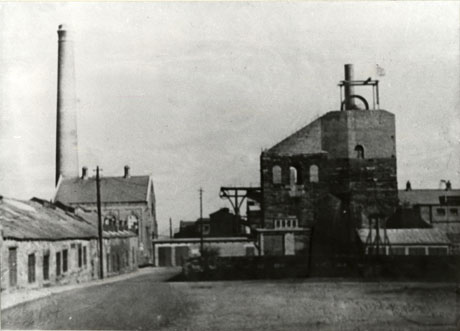 Photograph of a long low building on the left of the picture, with a taller building at its end with a tall chimney behind it; on the right of the picture is a tall building with winding gear and other lower buildings around it; the two blocks of buildings form the two sides of a square; they have been identified as Seaham Colliery, Knack High Pit
