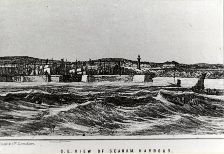 Photograph of an engraving of a harbour looking at it from the sea;in the foreground, are the waves and, beyond them, the walls of the harbour with sailing boats within; beyond the harbour are buildings and, beyond them, hills; it has been identified as Seaham Harbour; the picture has the caption: S. E. View of Seaham Harbour and the name Cook and Co., London