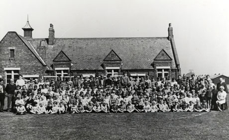 Photograph of a group of approximately a hundred children and approximately six adults posed outside a school, part of the facade and roof of which can be seen behind the group; they have been identified as pupils at High Colliery School, Seaham