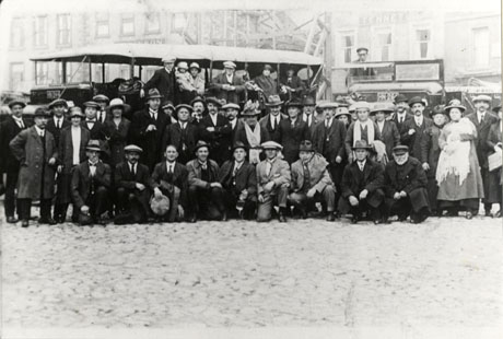 Photograph of approximately fifty people grouped in front of a motor charabanc in what appears to be an open space in a town; behind the charabanc are the facades of large buildings, possibly hotels or public houses; the word Tennet can be seen on one of them; behind the group is another motor vehicle with the registration number HN 264; the registration number of the charabanc may be HN 244; the group has been identified as a Buffs' outing from Seaham