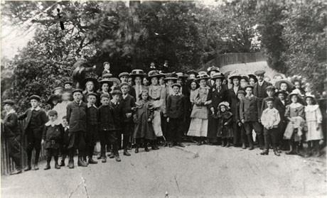 Photograph of a group of approximately fifty women and children and approximately two men, posed on a path leading up hill behind the group; there is a fence at the edge of the path on the left of the picture and there are large trees behind and to the side of the group; they are all dressed in suits and smart dresses; they have been identified as being on a Wesleyan Methodist Sunday School [Outing to] Jubilee Grounds