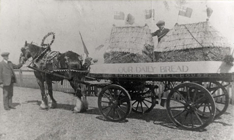 Photograph of a horse wearing decorations pulling a cart on which there are two small haystacks and a boy standing; the name, E. C. Snowden, is written along the cart; a man is standing at the horse's head; the photograph has been identified as Snowdon's Bakery Carnival Float in Seaham