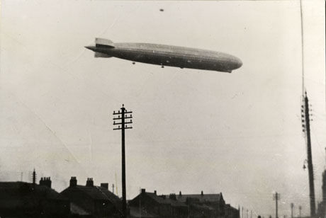 Photograph of a Zeppelin in the sky above the roofs of houses, which have been identified as Railway Street, Seaham