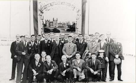 Photograph of twenty eight men in suits and ties posed in front of a miners' banner featuring a picture of the miners' convalescent home at Conishead Priory; they have been identified as Lodge Officials with First Banner, 1931; the following individuals have been identified: Joe Blackwell, Lodge Secretary, in the light suit in the centre of the photograph; Harry Oliver, second right on the front row; Bill Baty, third right on the front row
