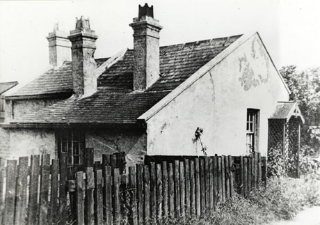 Photograph of the exterior of the back and side of a one storey cottage with a window and porch on the side wall and a window in the back wall; the roof, two chimney stacks and a wooden fence can also be seen; it has been identified as Toll Cottage, Seaham