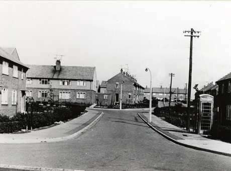 Photograph of the surface of a short road running away from the camera to a junction with another road; post-war two storey terraced houses line the roads; both the front and side of the houses can be seen; sodium street lights and a Gilbert Scott telephone box can be seen; the road has been identified as Derwent Close, Seaham