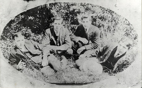 Photograph of four young men in suits and ties kneeling and lying on grass in front of trees; they are identified as four young Seaham miners in 1920