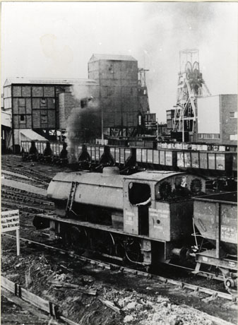 Photograph taken from above and behind of the steam locomotive Gamma with coal waggons and the winding gear, engine house and other buildings of Vane Tempest Colliery, Seaham, behind her; the date of the photograph has been identified as 1974