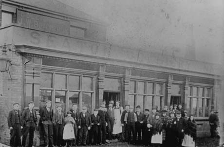Photograph of approximately twenty eight people standing outside a building with three large windows and two doorways; above the windows is a sign running the length of the building reading: Seaton Colliery Inn; the men are wearing suits and caps and the women aprons and shawls; the building has been identified as being re-named as The Phoenix at a later date and as being in Seaham