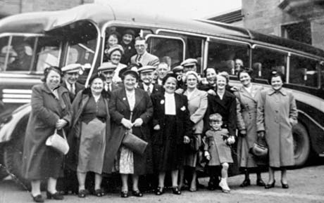 Photograph showing twenty men and women standing in front of, and in the entrance of, a single-decker bus; they are wearing suits and overcoats and a child, aged approximately four years, is with one of the women; they have been identified as Retired Miners, Wives, and Widows Trip, Seaham