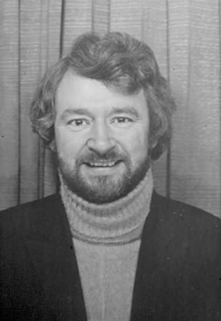 Photograph of the head and shoulders of a man with a beard and moustache, wearing a dark jacket and a roll-neck sweater, posed against curtains; he has been identified as Councillor Eddy Mason, Seaham