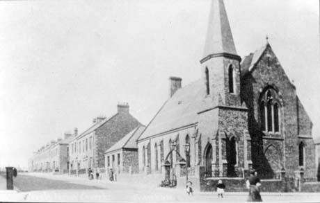 Photograph of the exterior of a church at the end of a street of blocks of houses, running away from the camera, the church is Gothic and has a tower on the corner; it has been described as the Presbyterian Church on Adolphus Street, Seaham, which has been described as having been bombed in the Second World War