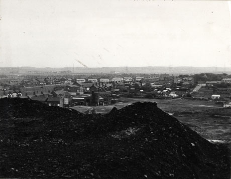 Photograph showing a panoramic view of Shotton, taken from the top of the pit heap, part of which forms the foreground of the picture; the view has an open space at the front with, possibly, colliery buildings, a playing field and a large light coloured building with three gables on the extreme left of the picture; in the distance are rows of terraced houses