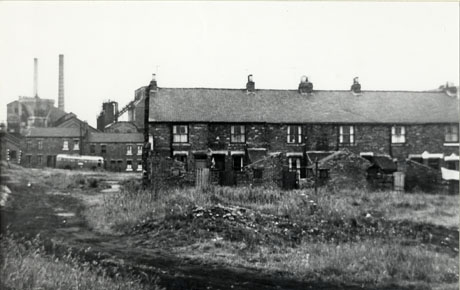 Photograph of the same view as in shot0030, but this photograph has been taken from a point closer to the colliery; most of the row of houses is in shot and the view of the colliery is different only in that part of the colliery building on the right is obscured by the roofs of the houses; a single decker bus is in front of the houses near to the colliery; the colliery is identified as Shotton Colliery
