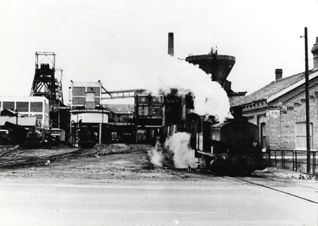 Photograph showing the buildings of Shotton Colliery with rail tracks running away from the camera to the colliery buildings; on the right of the picture, a locomotive is steaming towards the camera with a line of waggons behind; on the left of the picture, a locomotive can be discerned much further away steaming towards the camera