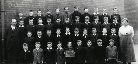 Photograph of forty one boys aged approximately ten years posed in front of a brick wall, accompanied by a man and a woman, presumably their teachers; a boy on the front row is holding a notice reading : Shotton Boys' School Standard VI 1919