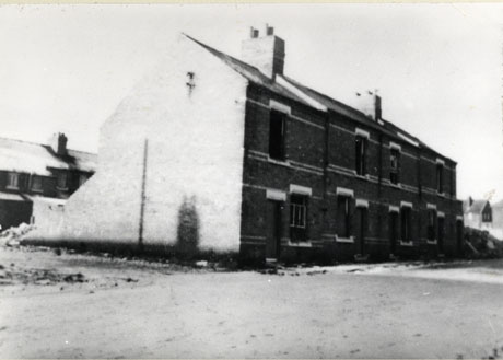 Photograph of the end and front of a terrace of five houses, standing on its own, surrounded by rough ground; behind, another terrace can be seen parallel to it; it has been described as Sheraton Street, Shotton, Just Before Demolition