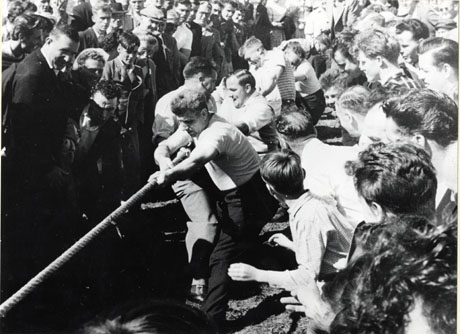 Photograph showing six men pulling a rope in a Tug of War, with crowds on either side of them; the event has been described as The First Annual Children's Sports Day at Shotton Colliery