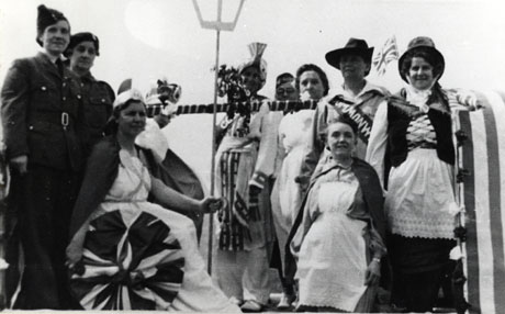 Photograph showing at the left of the photograph two women dressed in the uniform of the armed services; a woman dressed as Britannia with a shield and trident; a woman dressed as an Indian; a woman dressed in Welsh costume; and four other women in costume, presumably representing other countries of the British Empire; they have been identified as Shotton Colliery British Legion Tableau for Victory in Europe Day, 8 May 1945