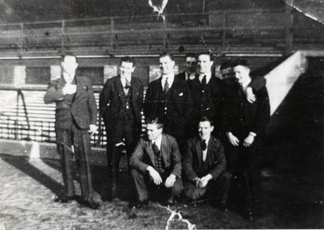 Photograph of a group of nine men in suits posed inside a football stadium; the photograph is indistinct, but the man at the centre of the back row has been identified as Tom Smith, a player with Sunderland Athletic Football Club