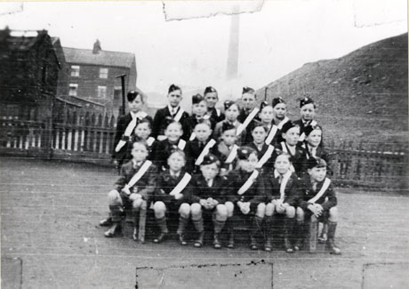 Photograph of a group of twenty two boys, aged approximately ten years, in a field with a pit heap on the right, and terraced houses on the left, behind them; the boys are in the uniform of the Church Lads' Brigade and are described as the Junior Training Corps of Shotton Colliery Church Lads' Brigade; they are celebrating Armistice Day, 1937