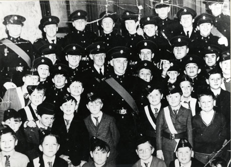 Photograph of a group of approximately fourteen men and twenty five boys in uniform described as members of Shotton, St. Saviour's Church Lads' Brigade, posed in front of a wall in an interior