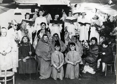 Photograph of the cast of a Nativity play performed by blind people, posed in front of the scenery; at the front are four adults and two boys dressed as shepherds and, behind them, the Three Kings and eight angels; the Virgin Mary is at the right of the picture; the play has been described as Shotton Colliery Charity Nativity play For The Blind