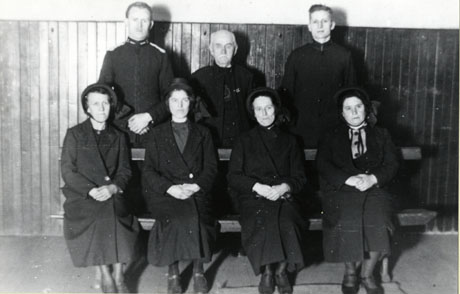 Photograph of three men standing behind four women sitting on a bench, inside a building; all of them are wearing Salvation Army uniform; they have been described as Salvation Army Census Board and have been identified as follows: Front Row: Mrs. Barraclough; Mrs. Lawson; M. Turnbull; Mrs. Alcock; Back row: Abel Tipling; Treasurer Walker; G. Wood