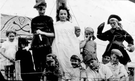 Photograph of twelve children, aged between approximately five and thirteen years, dressed as pirates; a mast to which a girl in a white garment is tied, is in the middle of the picture; a skull and cross bones is in the background; they have been described as Women's Institute Float - Peter Pan - Shotton