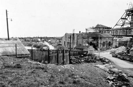 Photograph showing a fence and what may be allotments in the centre of the picture; on the right are the side of the buildings of a colliery with part of the winding gear in view; the colliery has been identified as Shotton Colliery