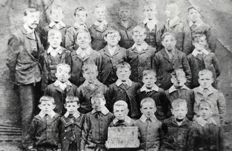 Photograph of twenty six boys, aged approximately eight years, standing in front of fabric, possibly that of a tent; a man,presumably their teacher, is standing on the left of the group; he has been identified as Mr. Henderson; the pupils have been identified as attending the boys' school in South Hetton
