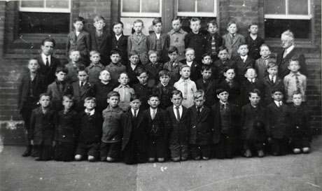 Photograph of a group of forty six boys, aged approximately ten years, against the wall of a building with long windows; on the left of the picture there is a young man and on the right a middle-aged man, identified as Mr. Lindsay; the children have been identified as being in South Hetton